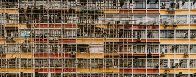 Dense bamboo scaffolding covers a Hong Kong residential tower, with balconies, windows and colourful façade bands visible